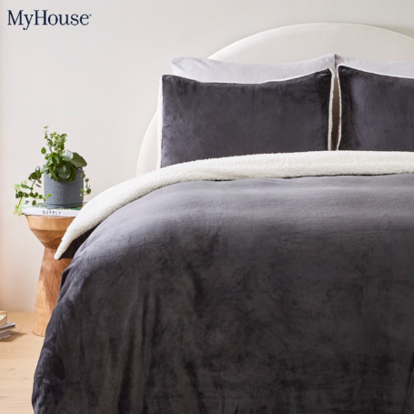 A bed with a charcoal quilt cover, matching pillows and a bedside table with a plant pot on it. Text 'MyHouse'