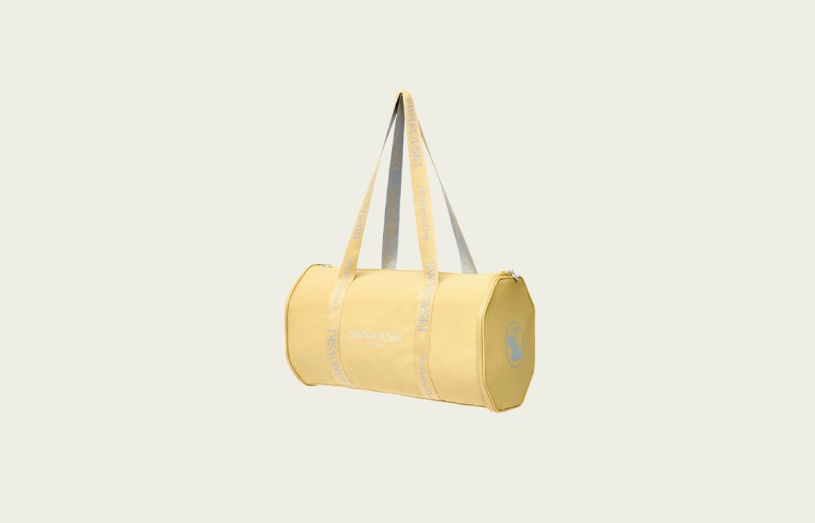 Image shows a yellow Swarovski overnight bag against a beige background